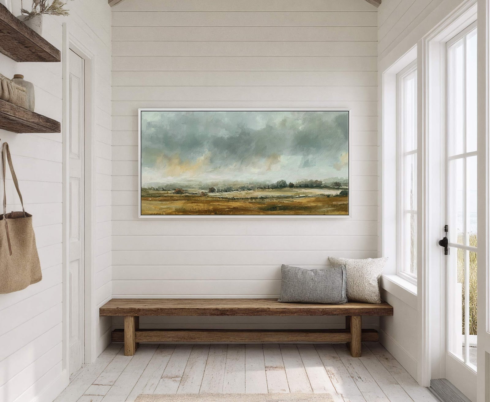 This horizontal canvas print features an impressionistic landscape painting with a muted palette of greens, golds, and grays. It hangs on a white paneled wall above a wooden bench with.