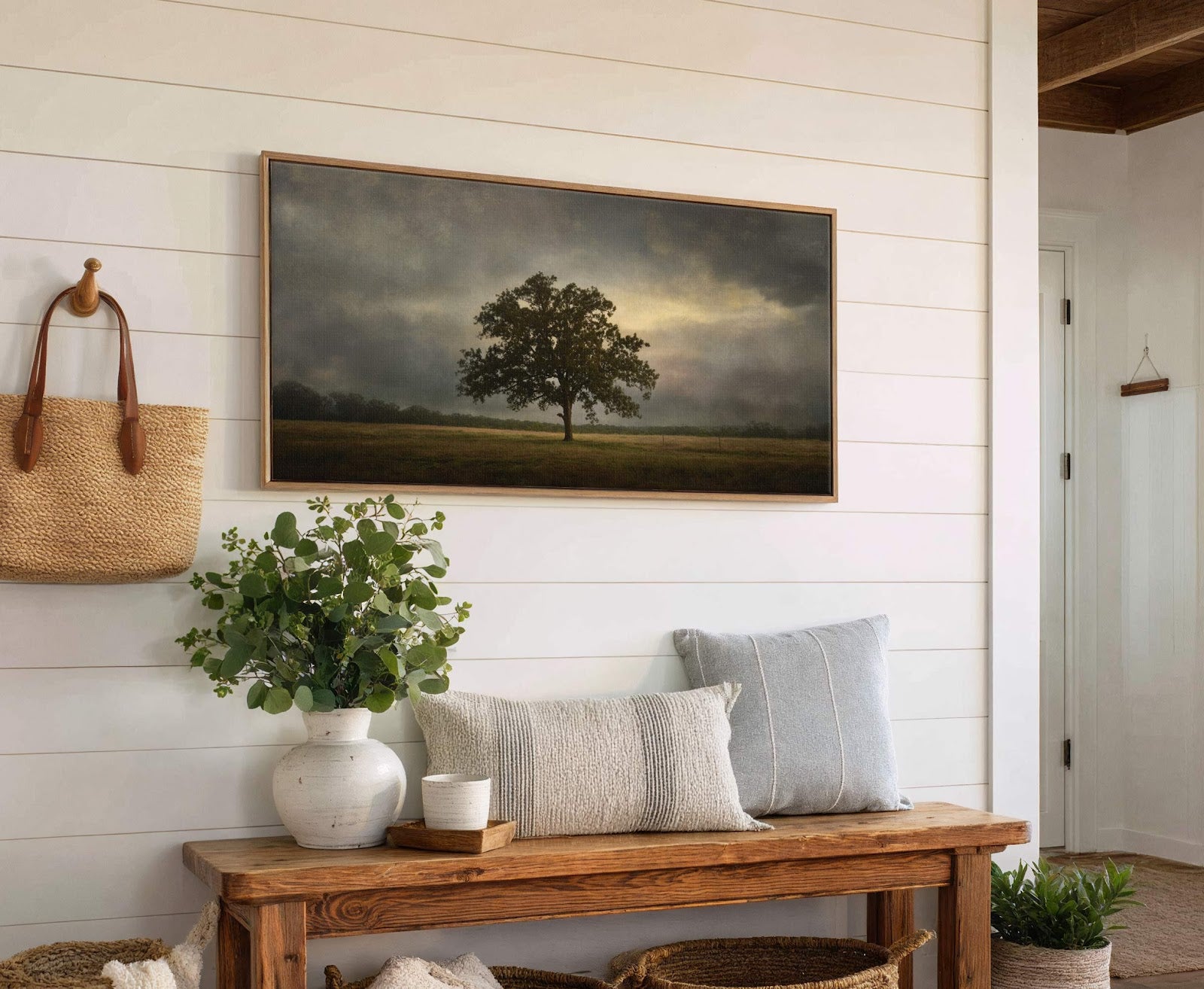 This horizontal canvas wall art features a lone oak tree in a field under dramatic, stormy skies, rendered in a moody palette and painterly style, displayed on a white shiplap.