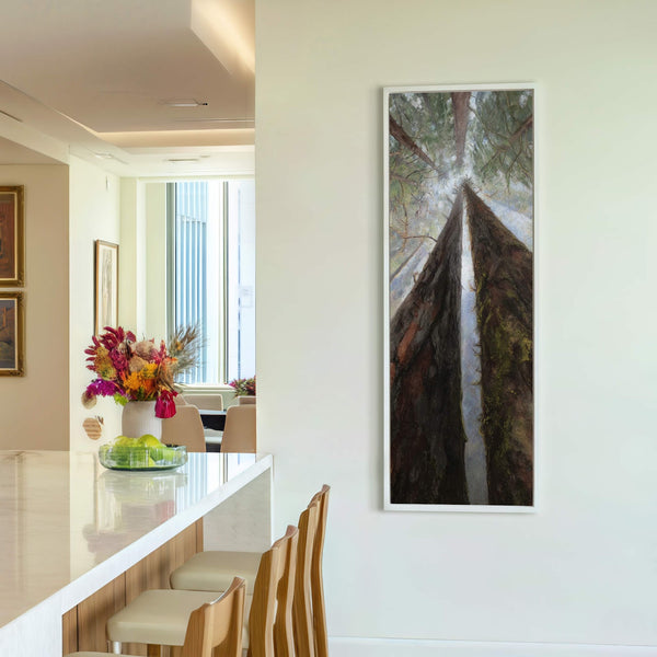 This vertical canvas wall art depicts a dramatic upward view of towering trees, with a palette of deep greens and browns. It hangs on a plain white wall above a.