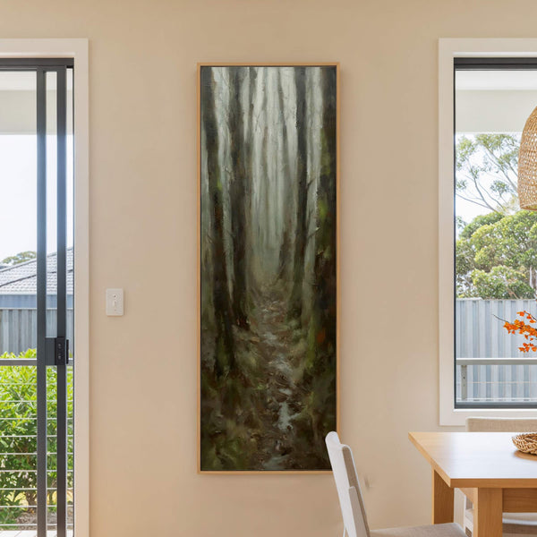 This vertical canvas wall art features an impressionistic forest scene with a muted green and brown palette, displayed on a beige wall next to a window and a wooden dining.