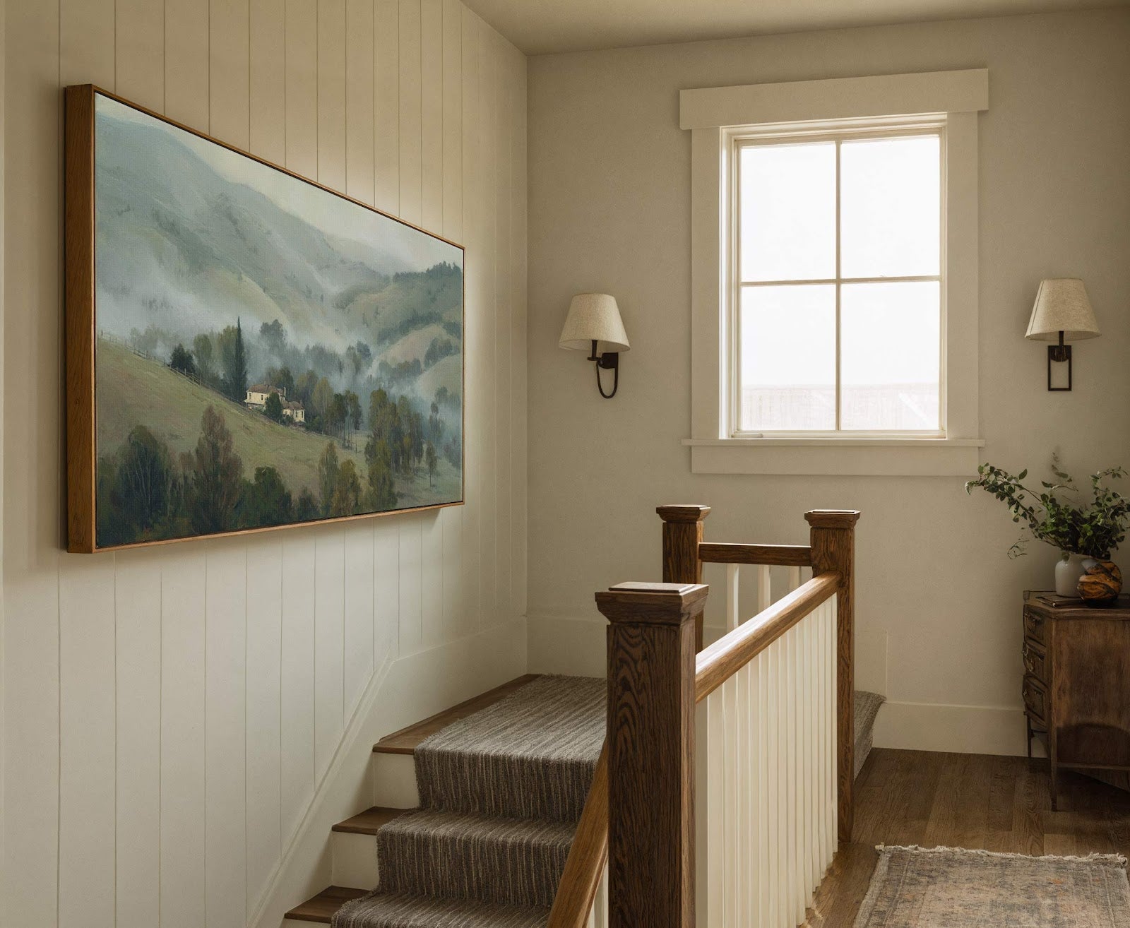 This horizontal canvas wall art features a serene landscape painting with a muted green and blue palette, depicting rolling hills, trees, and a house, framed in natural wood, displayed in.