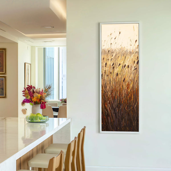 This vertical canvas wall art features an impressionistic painting of reeds and grasses in warm, earthy tones, framed in white and displayed on a neutral wall in a modern room.