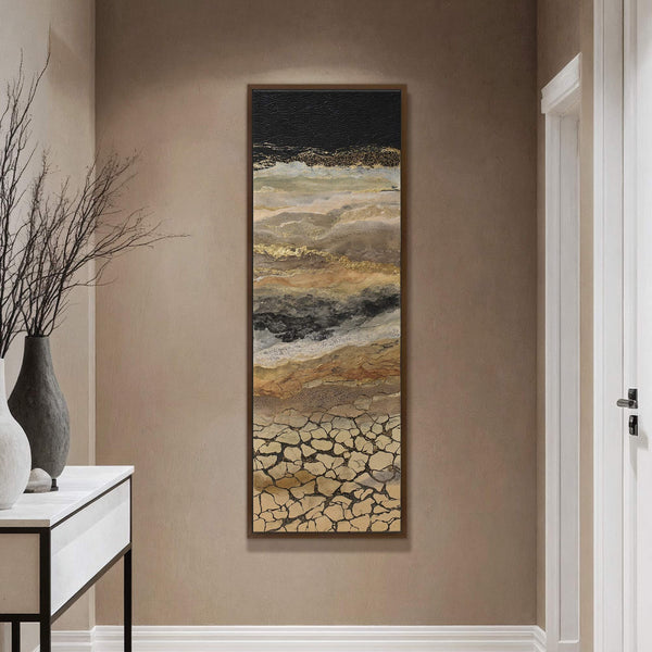 This vertical canvas wall art features an abstract landscape with a palette of earthy tones, black, and gold, framed in a natural wood finish, hanging on a beige wall next.