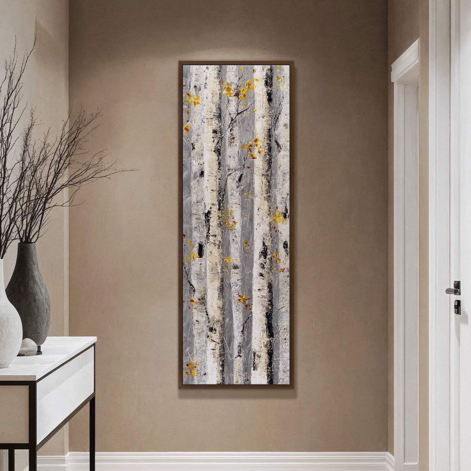 This vertical canvas wall art depicts an abstract birch tree forest with a palette of gray, white, black, and yellow accents, displayed on a tan wall above a console table.