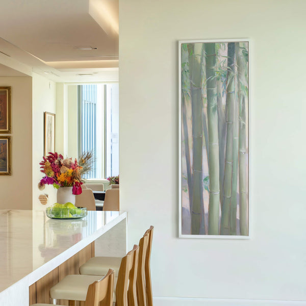 A vertical canvas wall art print depicts bamboo stalks in a soft, impressionistic style with a palette of greens and purples, framed in white and displayed on a light-colored wall.