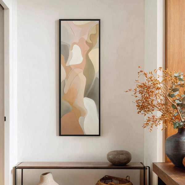 This vertical abstract art print features a soft palette of blush, cream, and gray tones within a black frame, hanging on a light-colored wall above a dark wood console table.