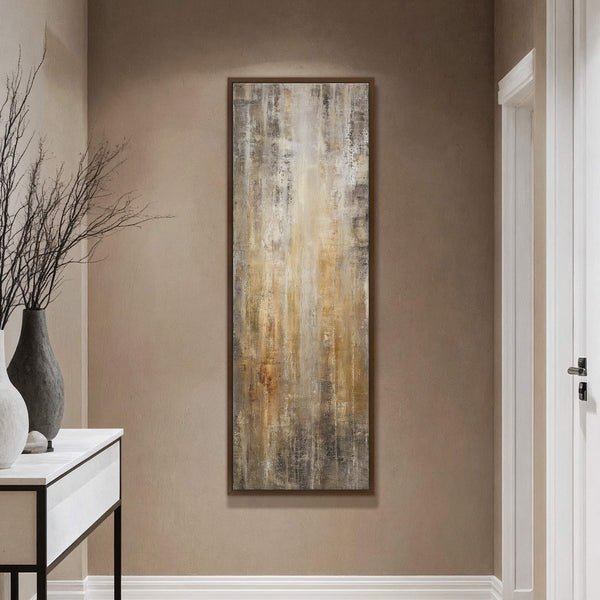This vertical canvas print features an abstract artwork with a palette of earthy browns, grays, and yellows, displayed in a hallway with a brown wall and a console table with.