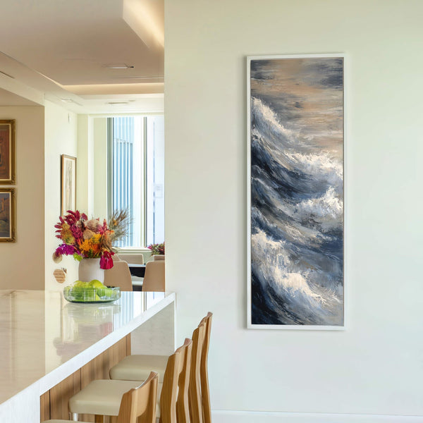 This vertical canvas wall art print features an abstract, impressionistic painting of crashing waves with a palette of blues, grays, and whites, framed in white, displayed on a pale wall.
