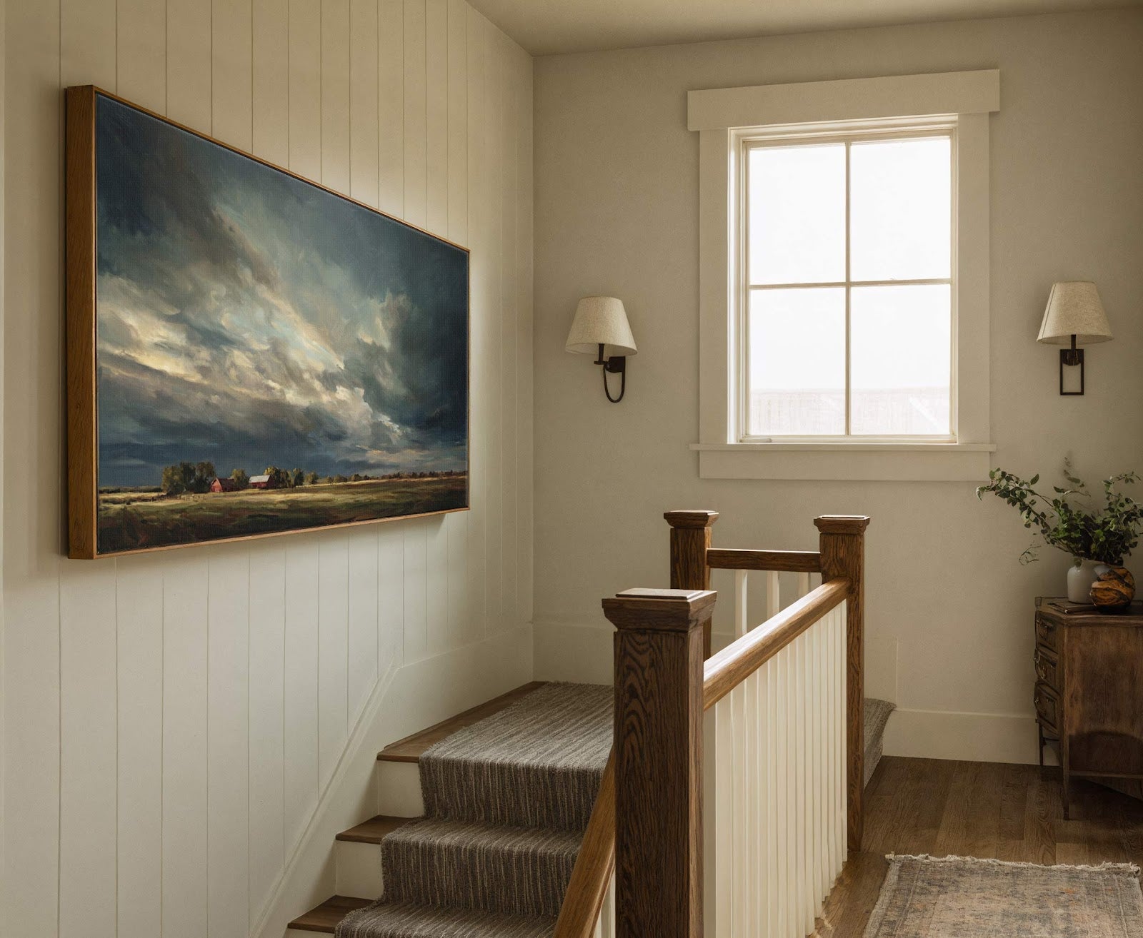 This horizontal canvas wall art features a dramatic, dark-sky landscape with red barns and fields, rendered in a painterly style with a muted palette, displayed above a staircase with paneled.
