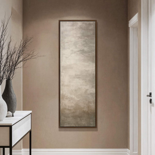 This vertical canvas wall art features an abstract landscape in a neutral palette, framed in dark wood, hanging on a taupe wall above a console table with vases and vase.