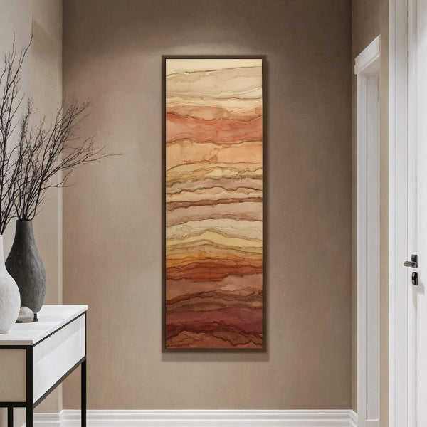 This abstract canvas wall art features a vertical orientation and a warm palette of reds, oranges, and beiges. It is framed in a dark wood and hangs on a taupe.