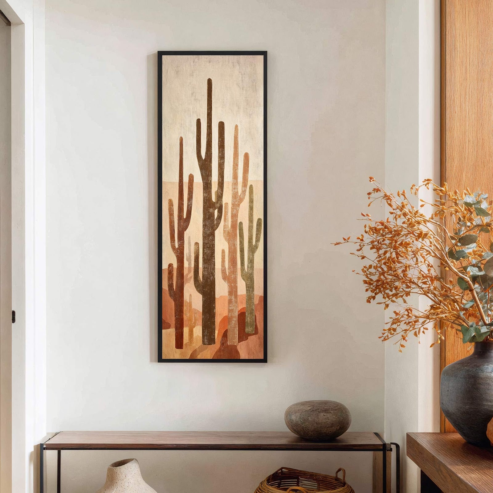 This vertical, abstract art print features a desert landscape with various cacti in warm earth tones of brown, orange, and beige, framed in black, hanging above a wooden console table.