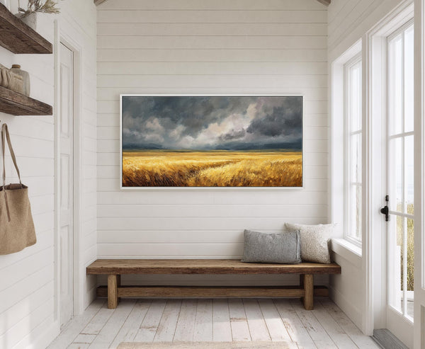 This horizontal canvas print captures a golden wheat field under a dramatic, cloudy sky in an impressionistic style. It hangs in a room with white paneled walls above a rustic.