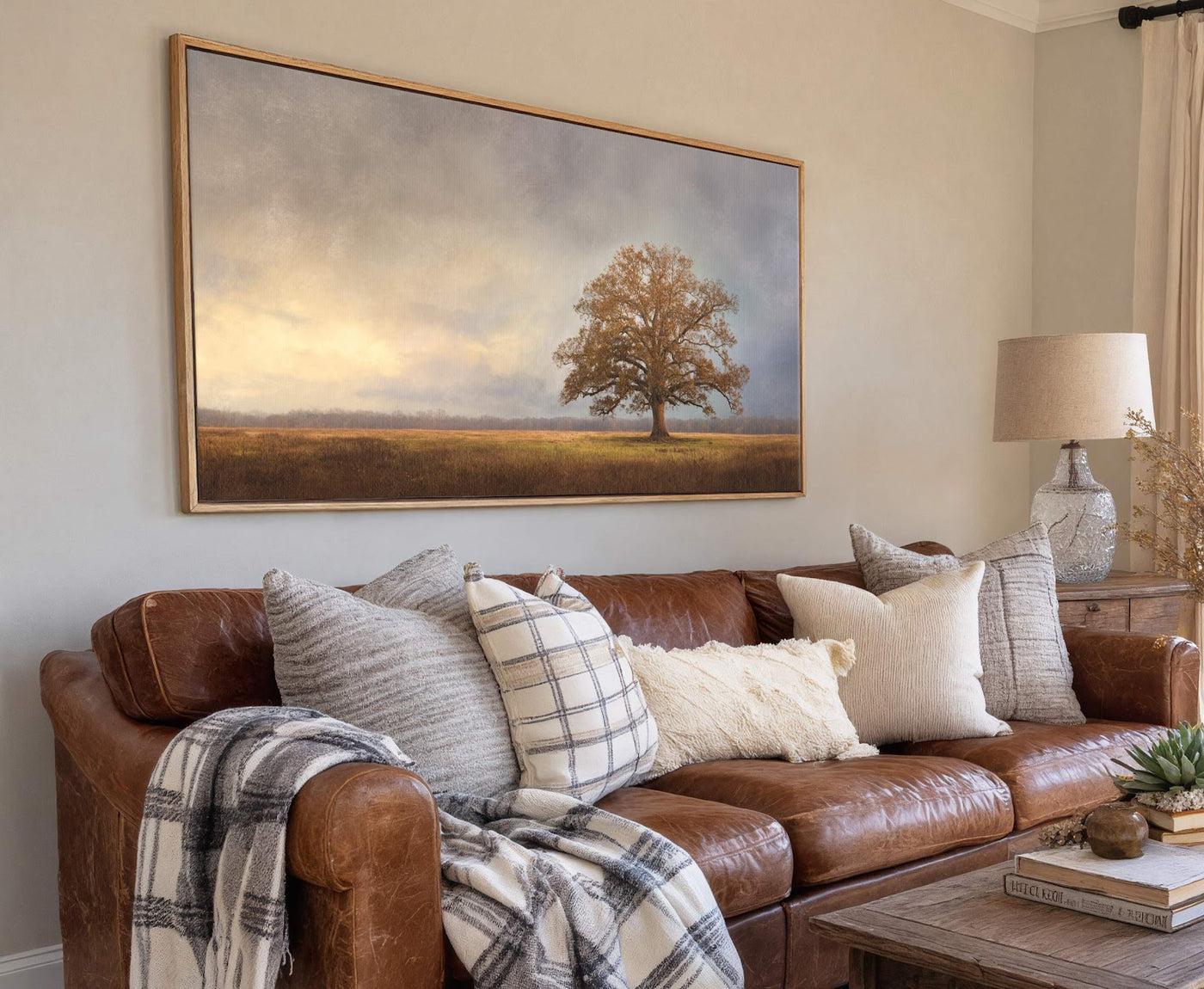 This horizontal, stretched canvas wall art features a beautiful, rustic painting of a single, large tree in a grassy field under a dramatic, cloudy sky. The artwork is displayed in.