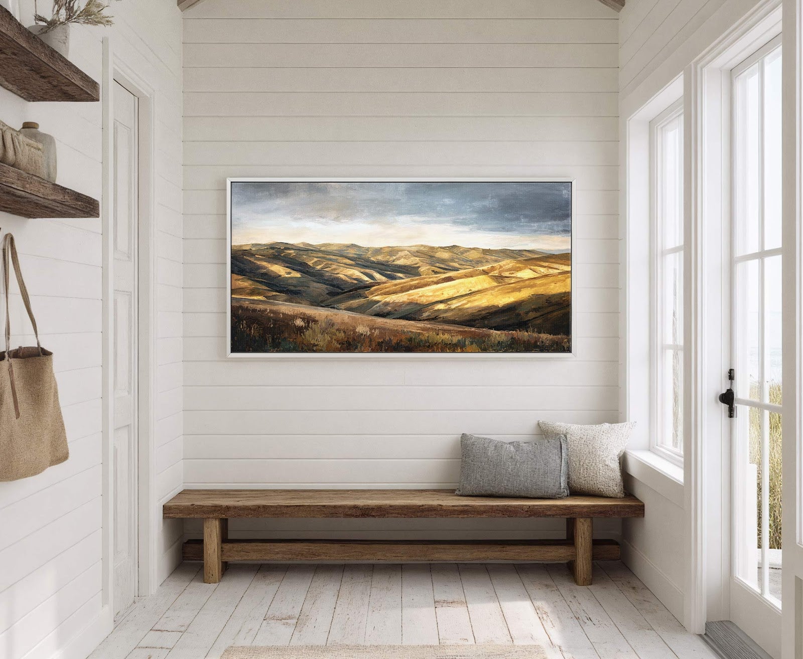 This horizontal canvas print depicts rolling hills in a painterly style with a warm, golden-brown palette. It is displayed on a white shiplap wall in a hallway with a rustic.