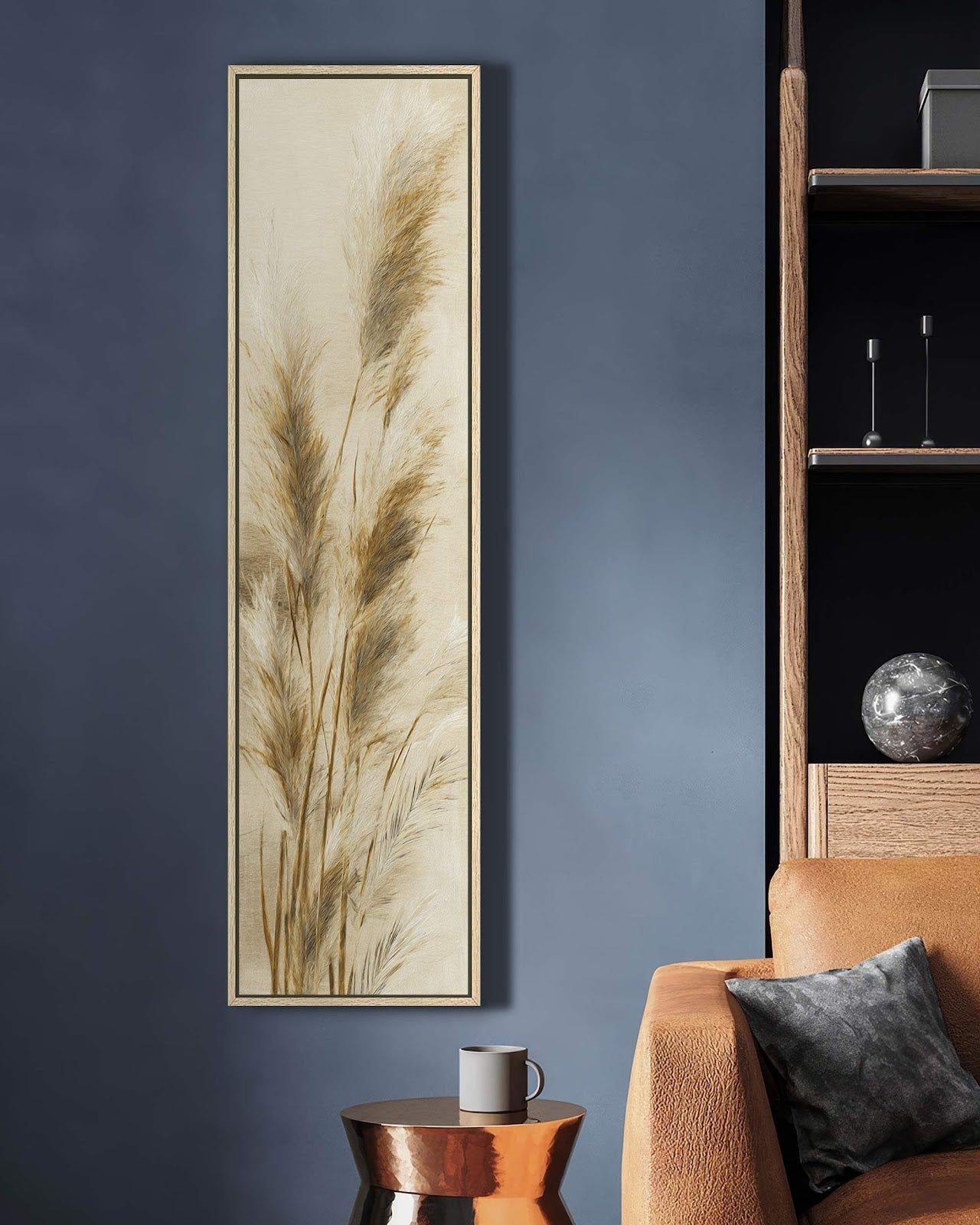 This vertical botanical art print features neutral pampas grass in a natural floater frame, displayed on a navy blue living room wall beside a tan leather sofa.