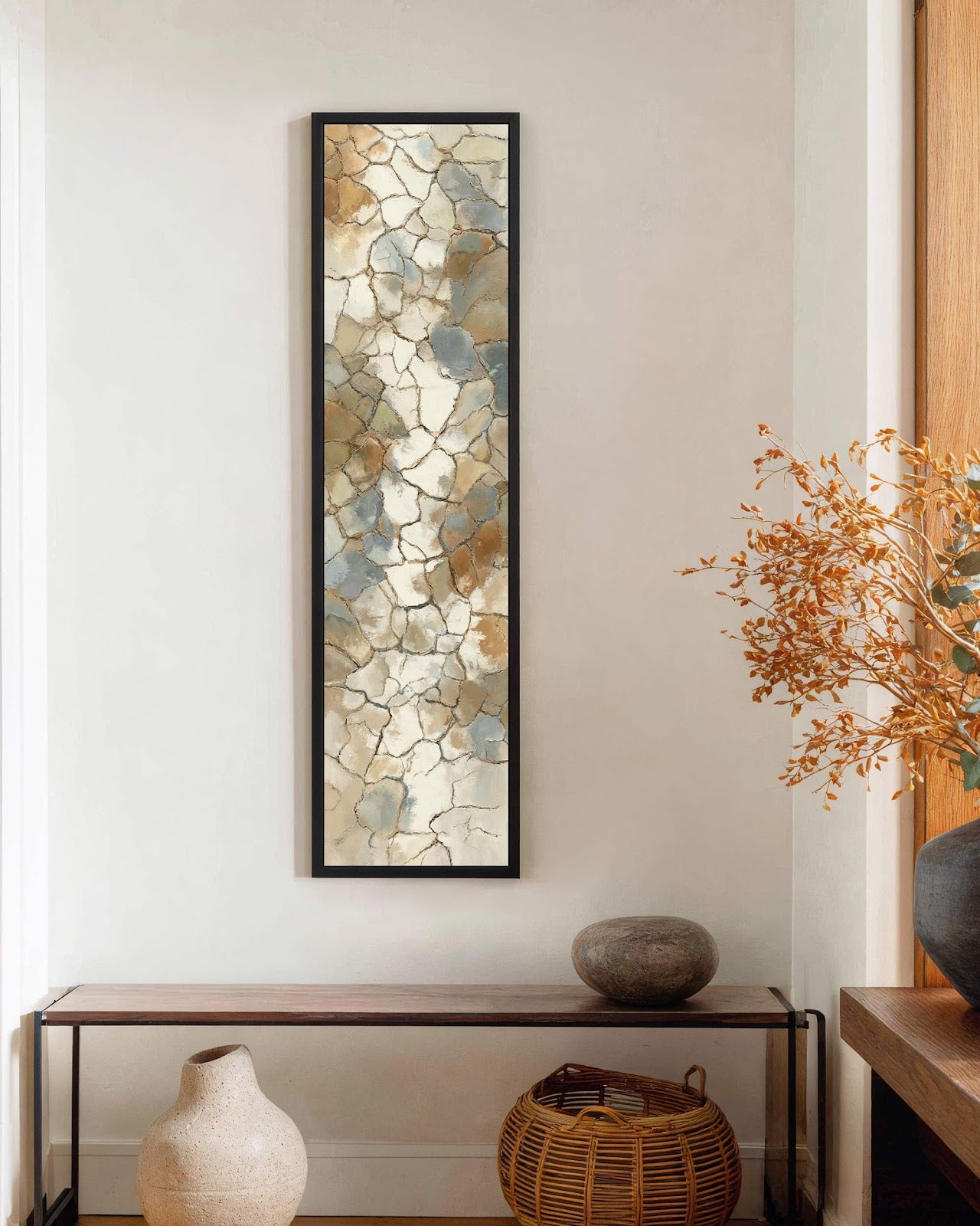 This vertical abstract art print showcases an earth-toned, cracked-pattern motif in a black floater frame, mounted on a white hallway wall above a sleek wooden console table.