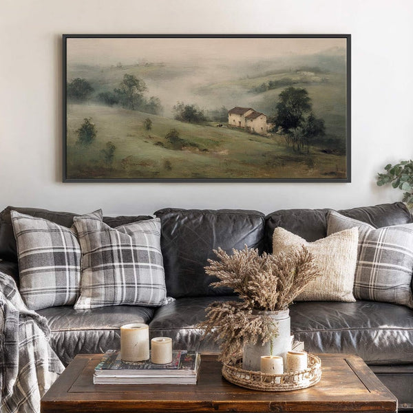 This horizontal canvas print features a hazy landscape with muted green and earth tones, depicting a farm with two houses nestled in rolling hills. It is displayed above a dark.