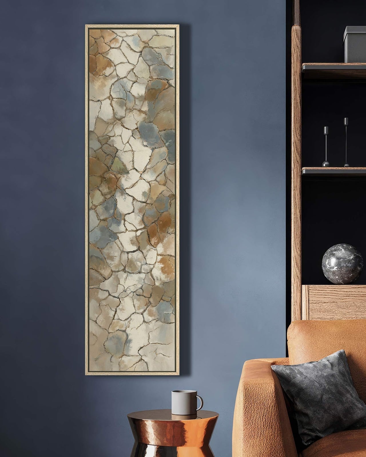 This vertical art print features an abstract earth-toned mosaic pattern in an oak floater frame, hanging on a navy wall in a living room beside a tan leather sofa.