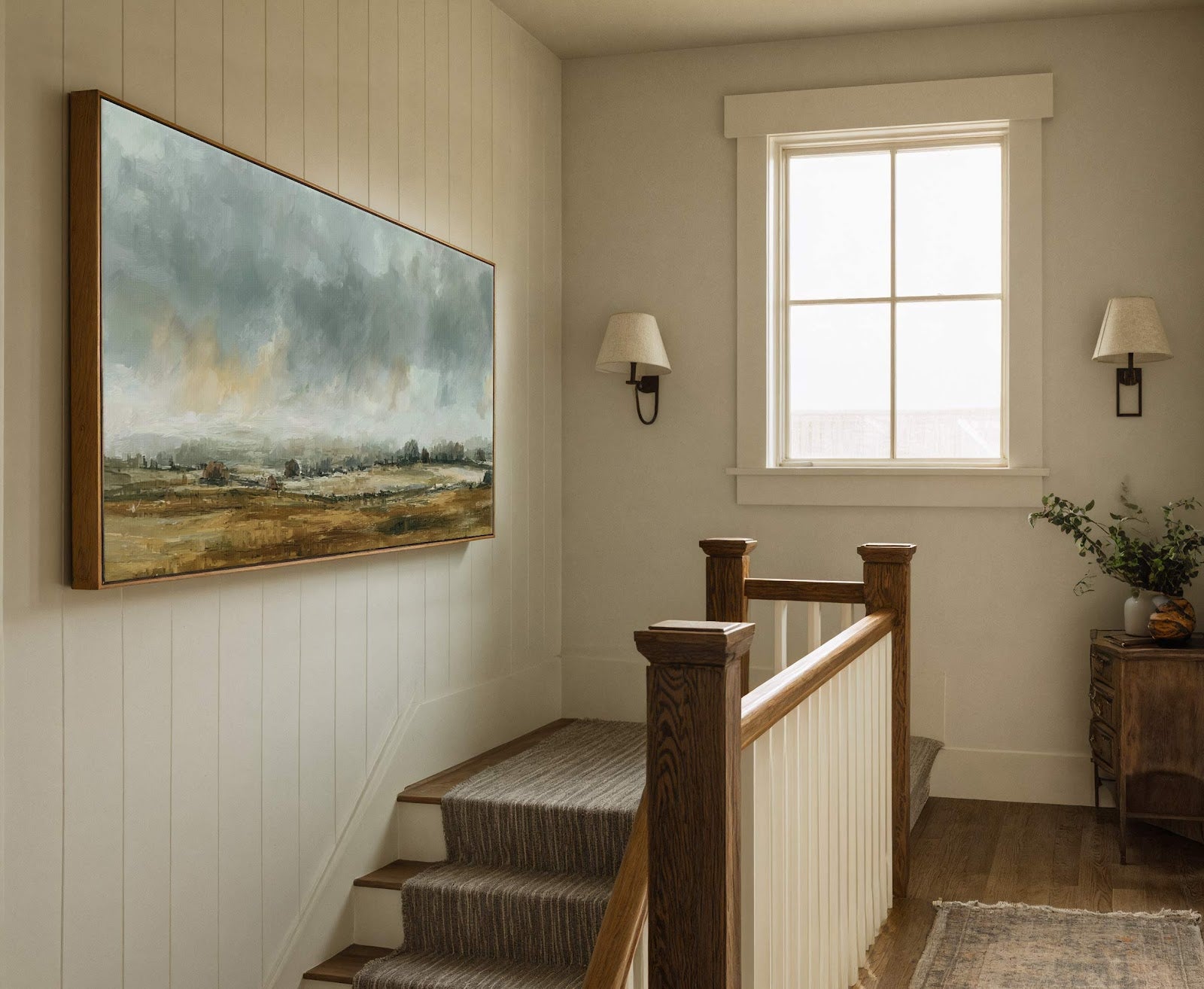 This horizontal canvas wall art features an impressionistic landscape in a muted earth-toned palette, set against paneled walls near a staircase and a rustic wooden console table.