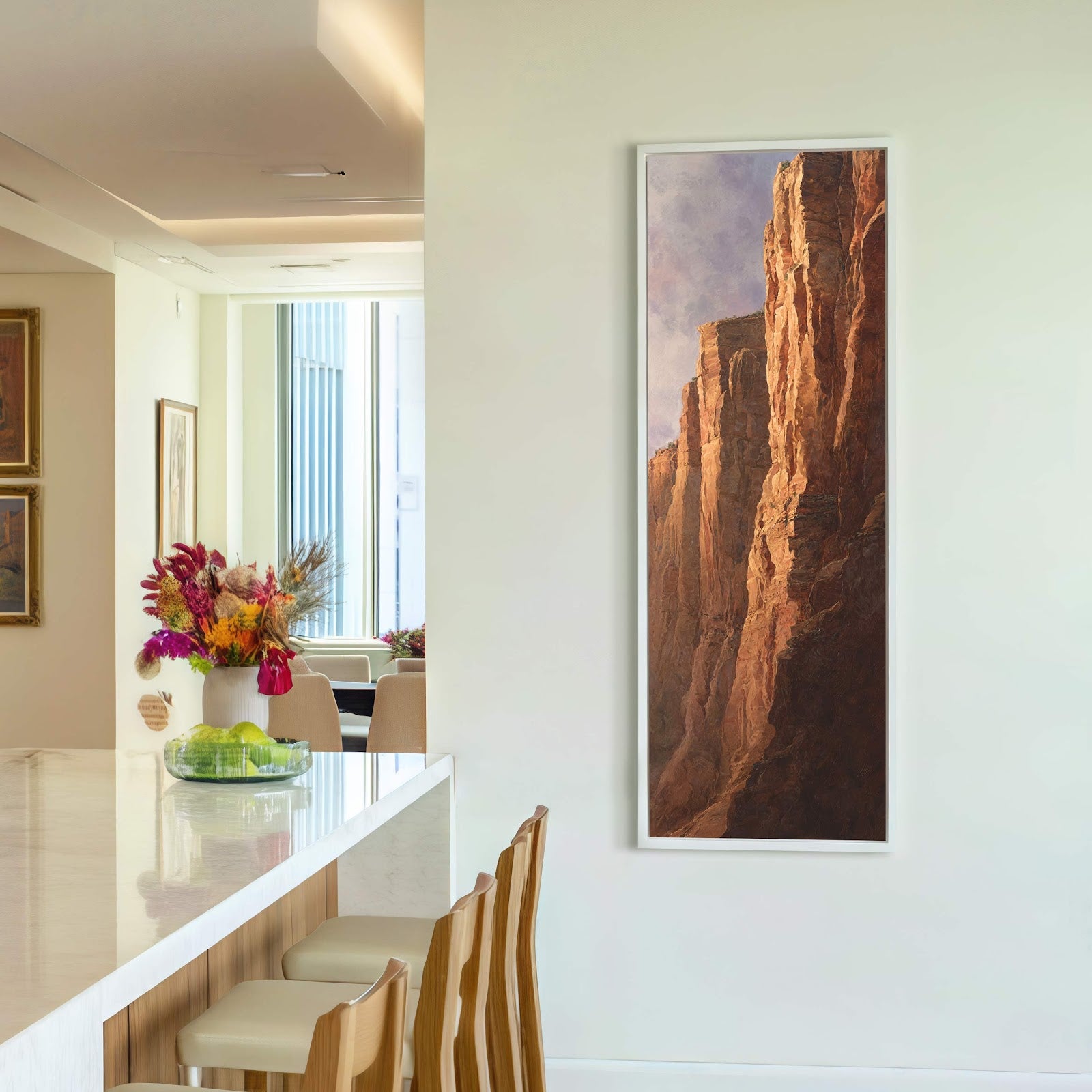 This vertical canvas wall art depicts dramatic, sunlit cliffs in earthy tones, framed in white, and hangs on a pale wall next to a window in what appears to be.