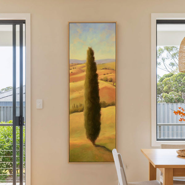 This vertical canvas wall art features a tall, dark cypress tree against a warm, impressionistic landscape with a palette of yellows, oranges, and blues, framed by a natural wood floater.