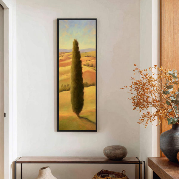This vertical canvas print features a Tuscan landscape with a prominent cypress tree, rendered in warm, golden tones and a painterly style. It hangs on a white wall above a.