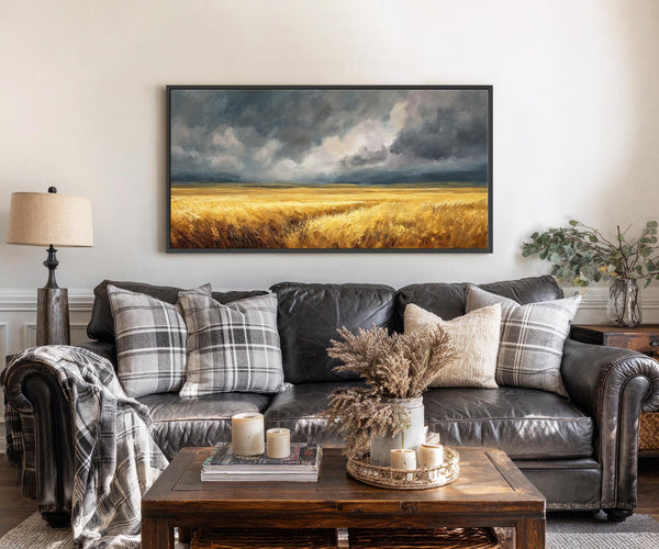 This horizontal canvas wall art features a dramatic oil painting of a golden wheat field under dark, stormy clouds with a warm palette. It is displayed above a black leather.