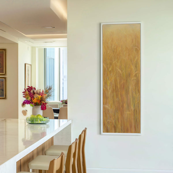 This vertical canvas print features an impressionistic painting of golden wheat stalks in warm yellow and orange tones. The artwork is displayed on a white wall in a room with.