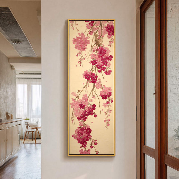 This vertical canvas wall art displays a branch of pink and deep red cherry blossoms with a gold frame, set against a neutral wall with a glimpse of a kitchen.