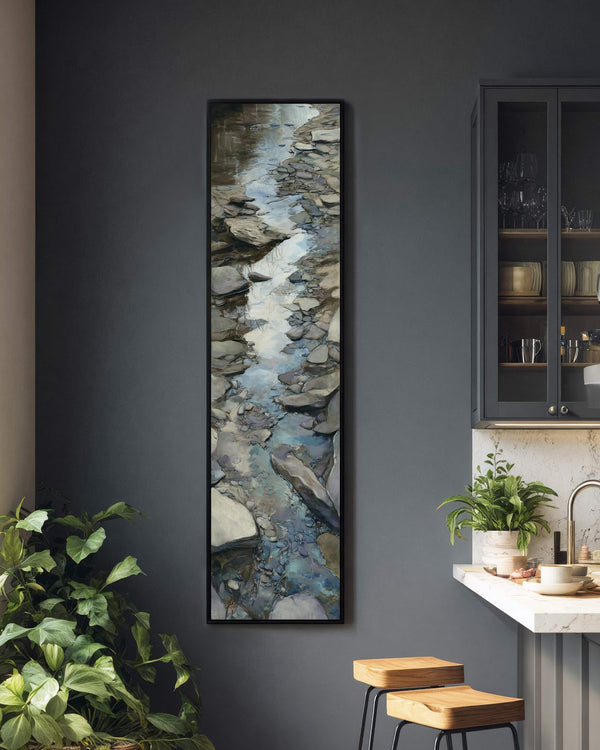 This vertical art print of an impressionistic rocky stream in muted earth tones hangs in a black floater frame on a dark gray kitchen wall near a sleek cabinet.