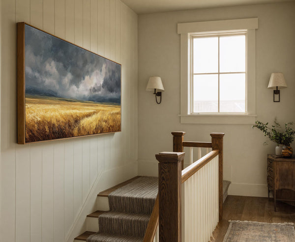 This horizontal canvas wall art features a dramatic landscape with a stormy sky over a golden field, rendered in a painterly style. It is displayed on a paneled wall above.