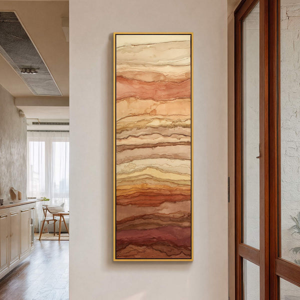 This vertical, abstract canvas wall art features layered earth tones in a style resembling flowing ink. It is framed in a thin gold floater frame and hangs on a neutral.