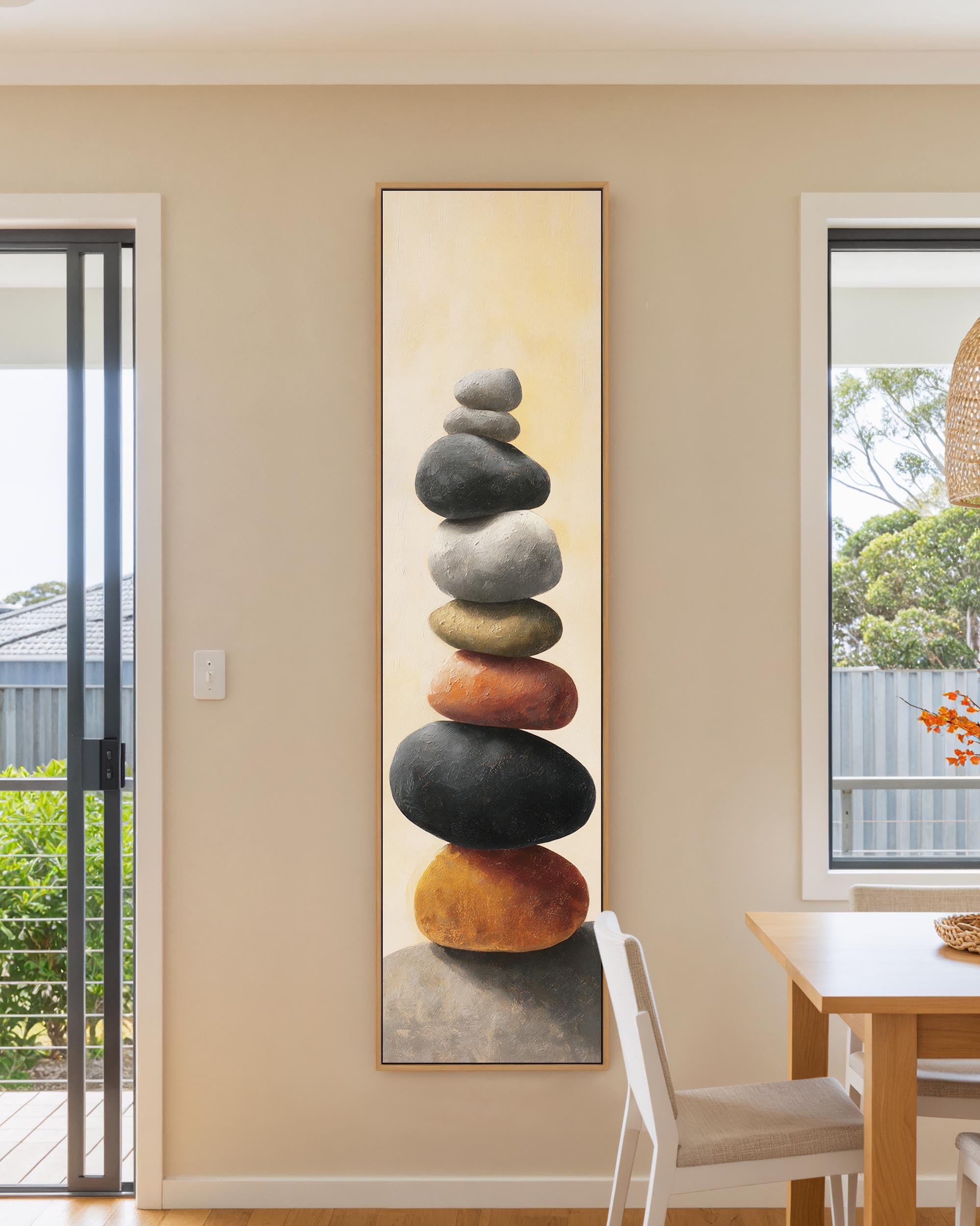 Tall vertical framed canvas wall art featuring a painting of balanced, stacked Zen stones in grey, black, rust, and gold tones on a warm beige background.