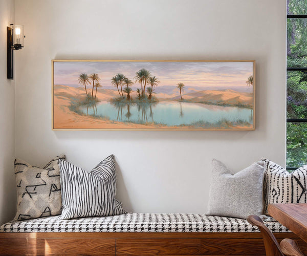 Framed desert oasis canvas wall art hung above a patterned bench in a modern interior with neutral cushions and natural light