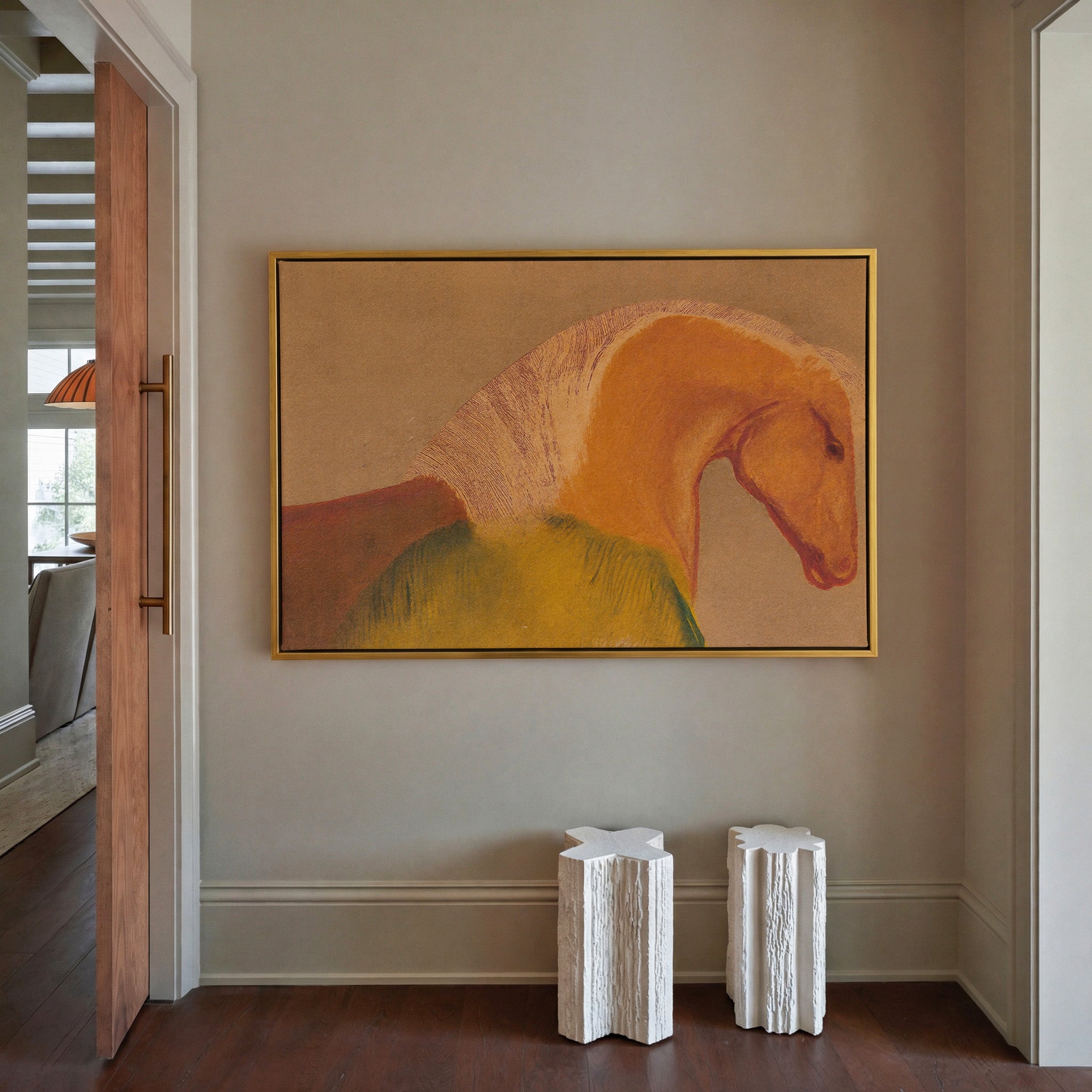 Abstract horse portrait canvas print in gold floater frame hung in a warm taupe entryway — close-cropped equine figure in amber, burnt sienna, and deep olive green against a sandy brown ground, styled above two white sculptural side tables on dark hardwood floors