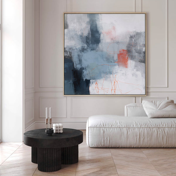 Large natural framed abstract art print featuring energetic brushstrokes and layered shapes in shades of deep blue, light blue, grey, white, and striking rust orange, displayed above a white modular sofa and fluted black coffee table in a modern living room with neutral walls