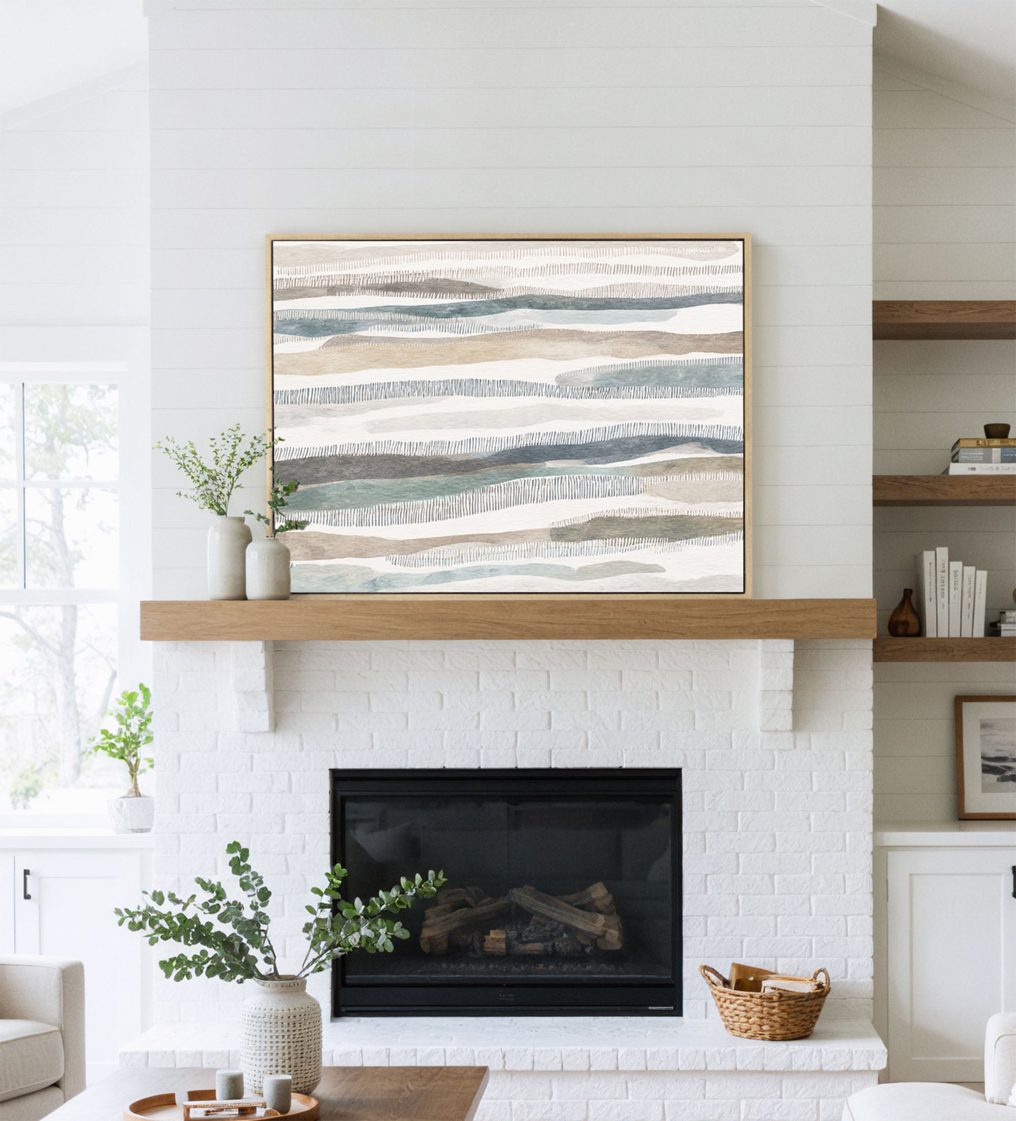 Large abstract art with horizontal bands of muted blues, browns, and grays hanging above a white brick fireplace.