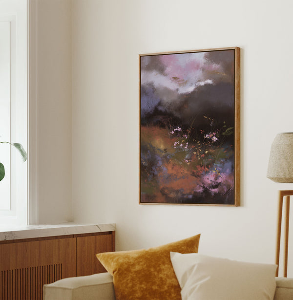 Pecan framed abstract painting featuring vibrant clusters of pink, purple, red, orange, and yellow flowers in a dark, atmospheric meadow under a dramatic, colorful sky, hung on a light wall above a sofa