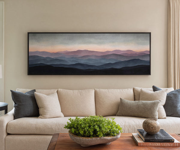 Framed mountain sunset canvas wall art displayed above a beige sofa in a modern living room with neutral decor and accent pillows.