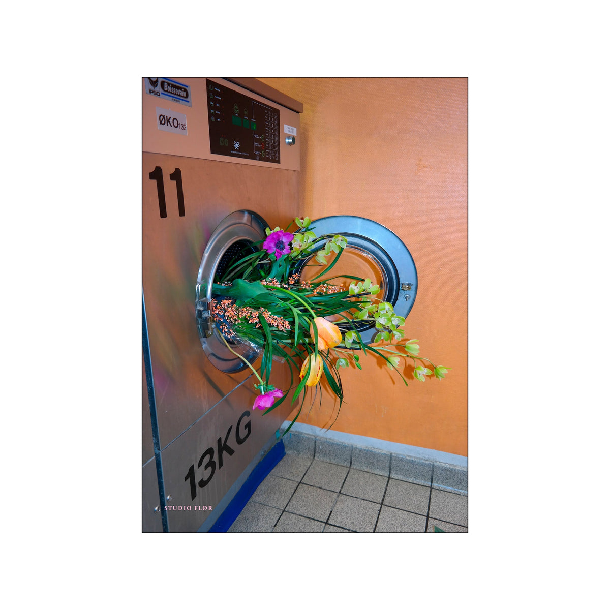 Open washing machine filled with colorful flowers against an orange wall and tiled floor