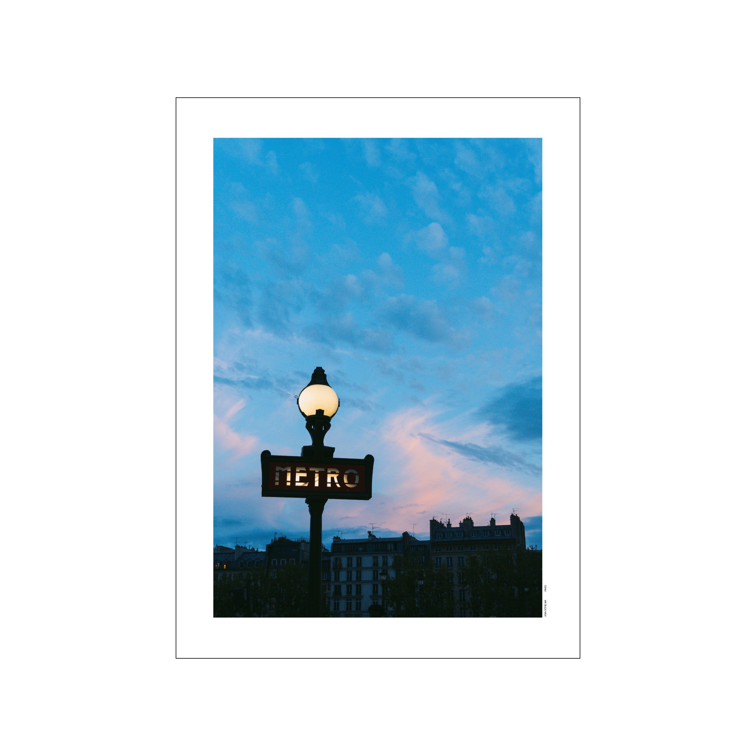 An iconic Parisian Metro sign illuminated at dusk, set against a dramatic sky with soft pink and deep blue clouds, hinting at urban beauty and romantic evenings.