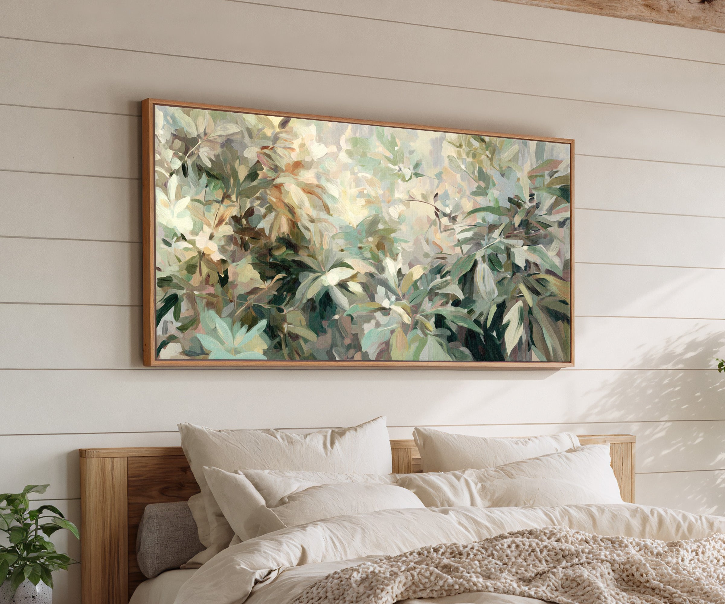 lush layered foliage in soft green, cream, and canvas wall art in an oak frame above a bed