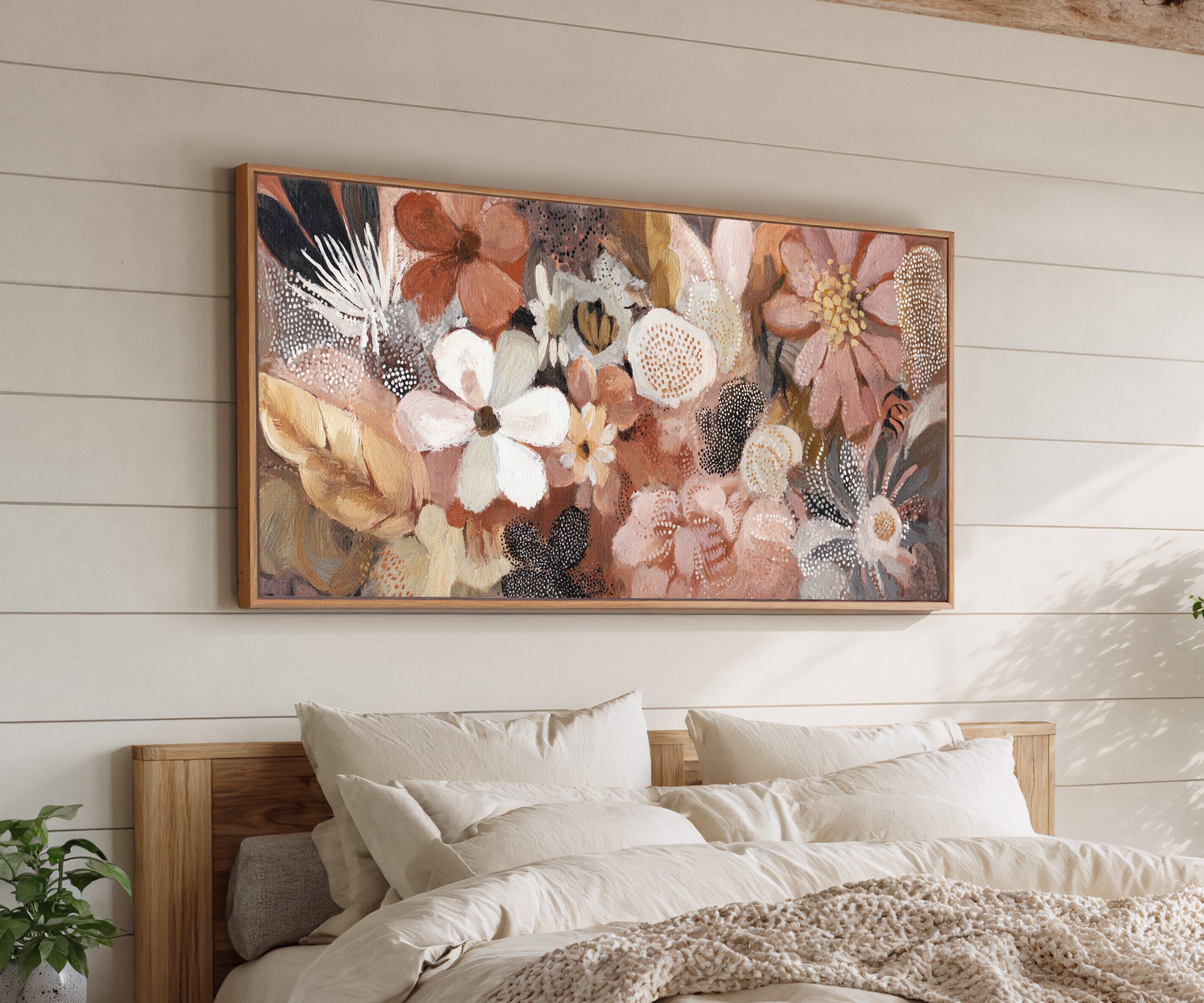 densely packed rounded flowers in blush, rust, canvas wall art in an oak frame above a bed