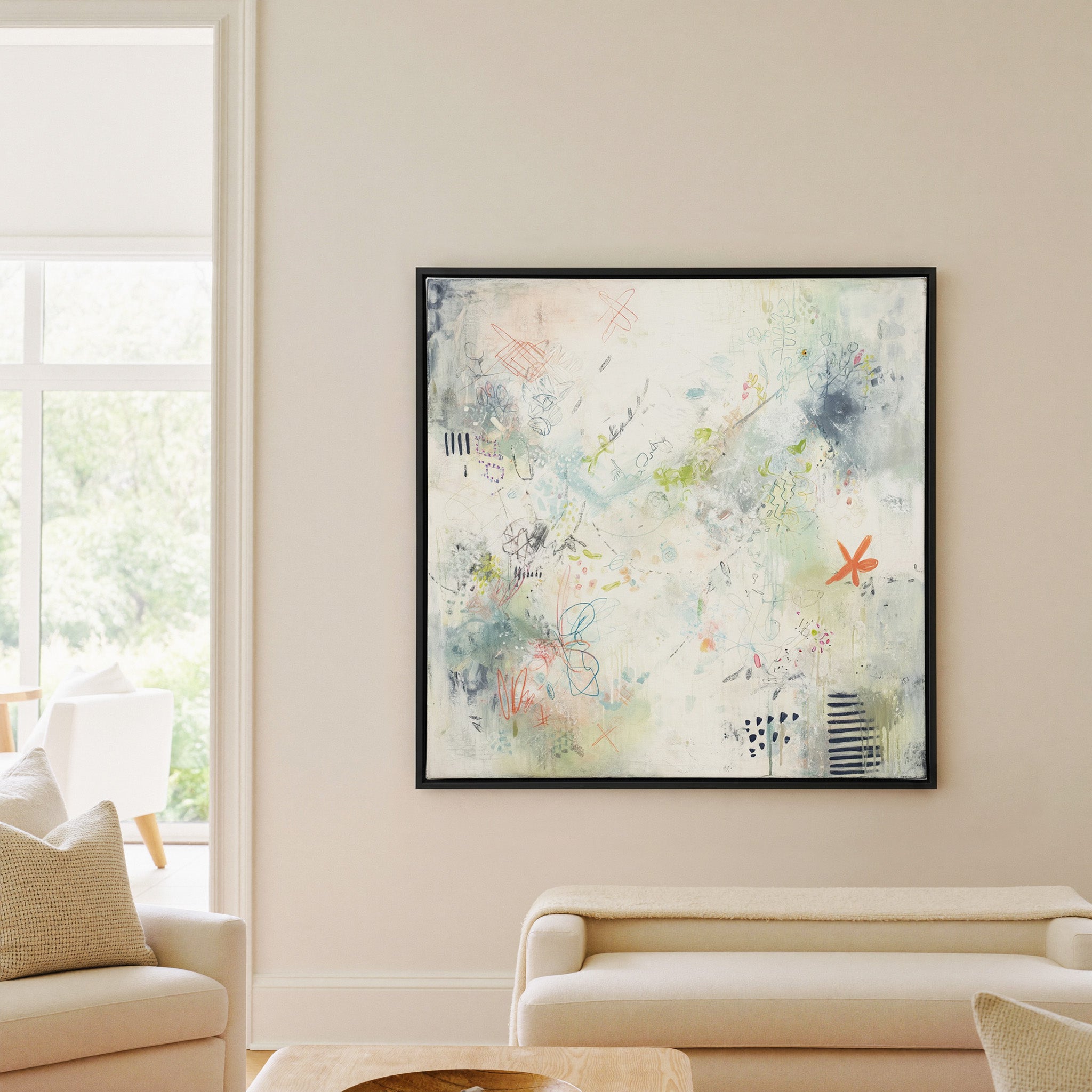 airy cream abstract with pastel doodles and canvas wall art in a black frame in a living room
