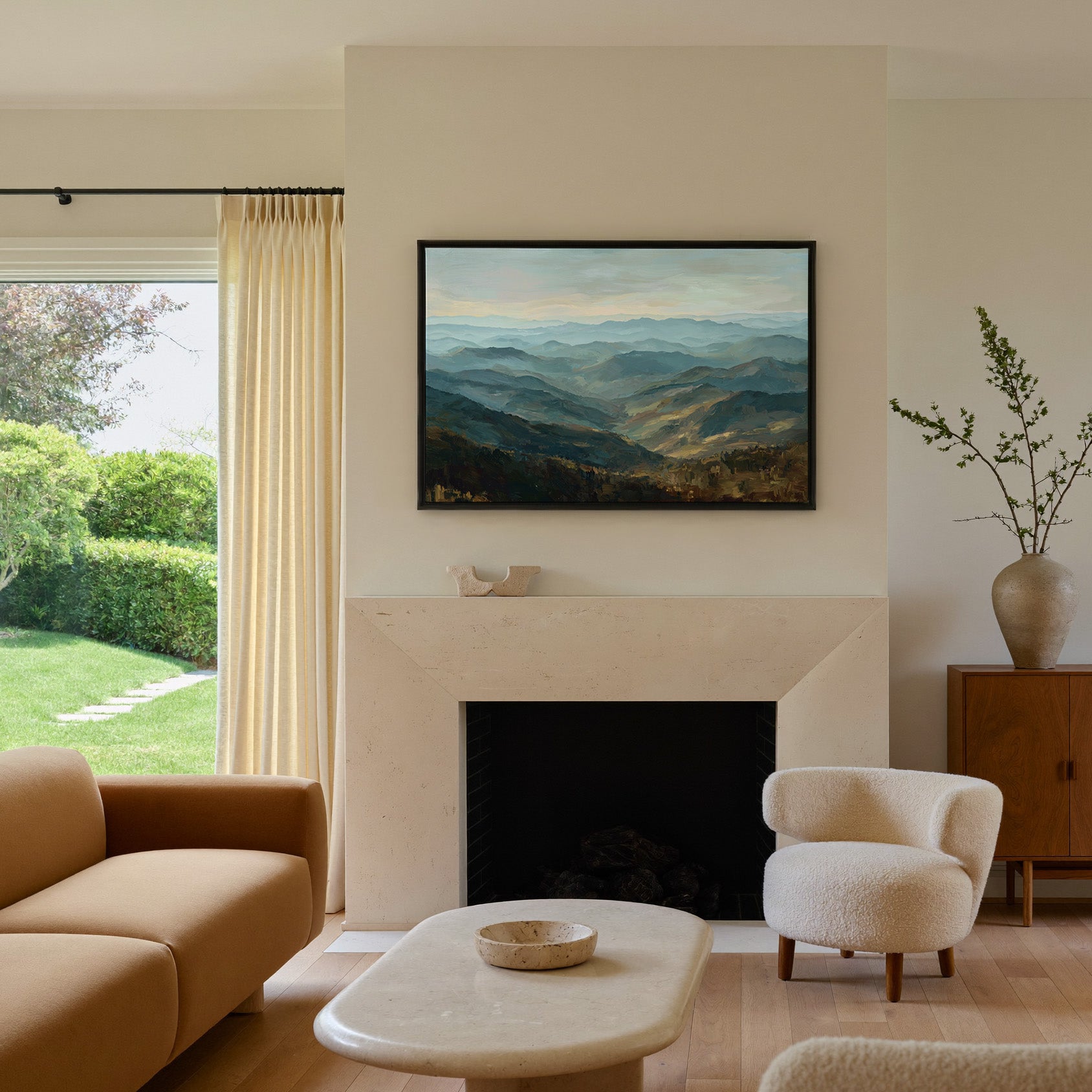 layered blue ridgelines with pale sky and warm canvas wall art in a black frame above a mantel