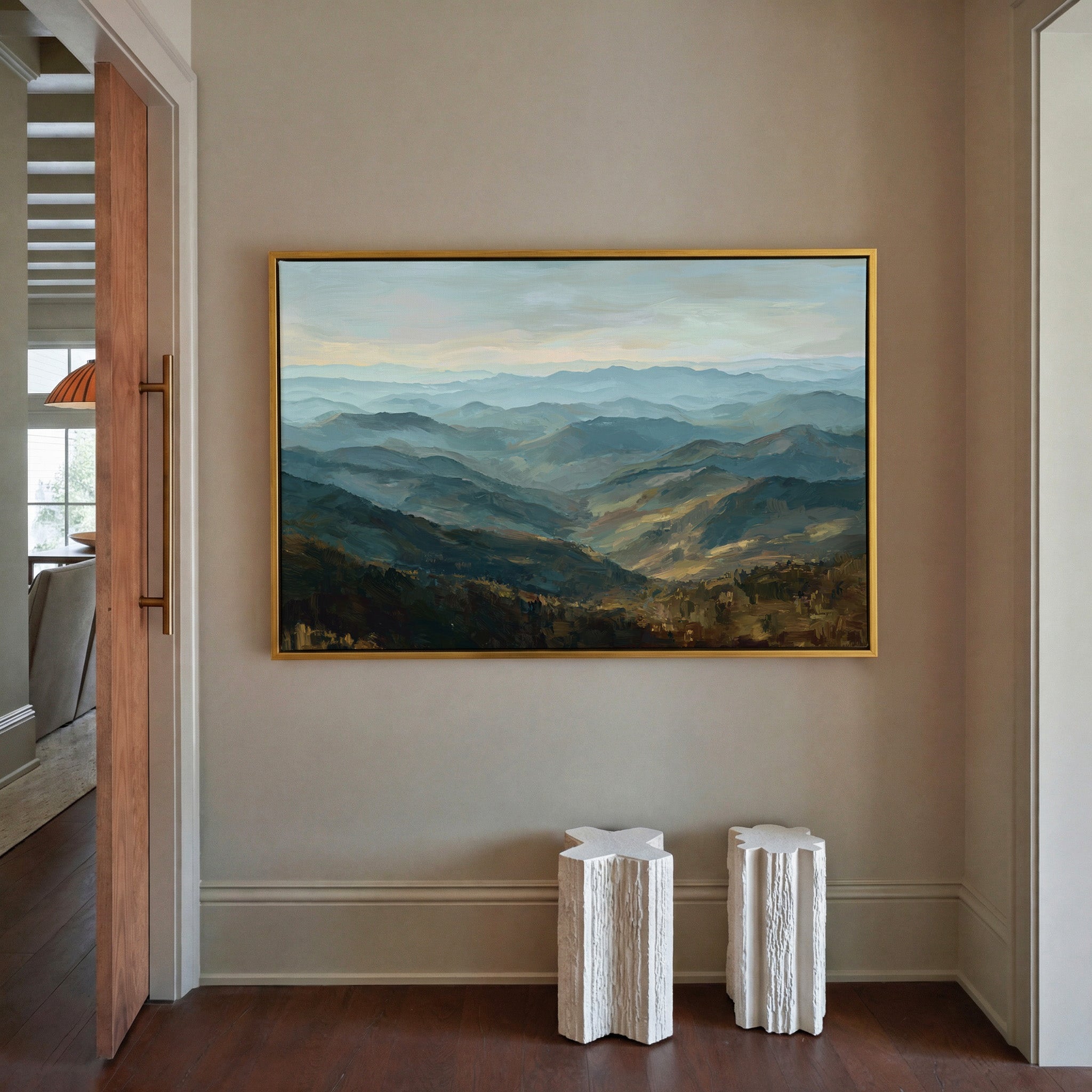 layered blue ridgelines with pale sky and warm canvas wall art in a gold frame in a styled room setting