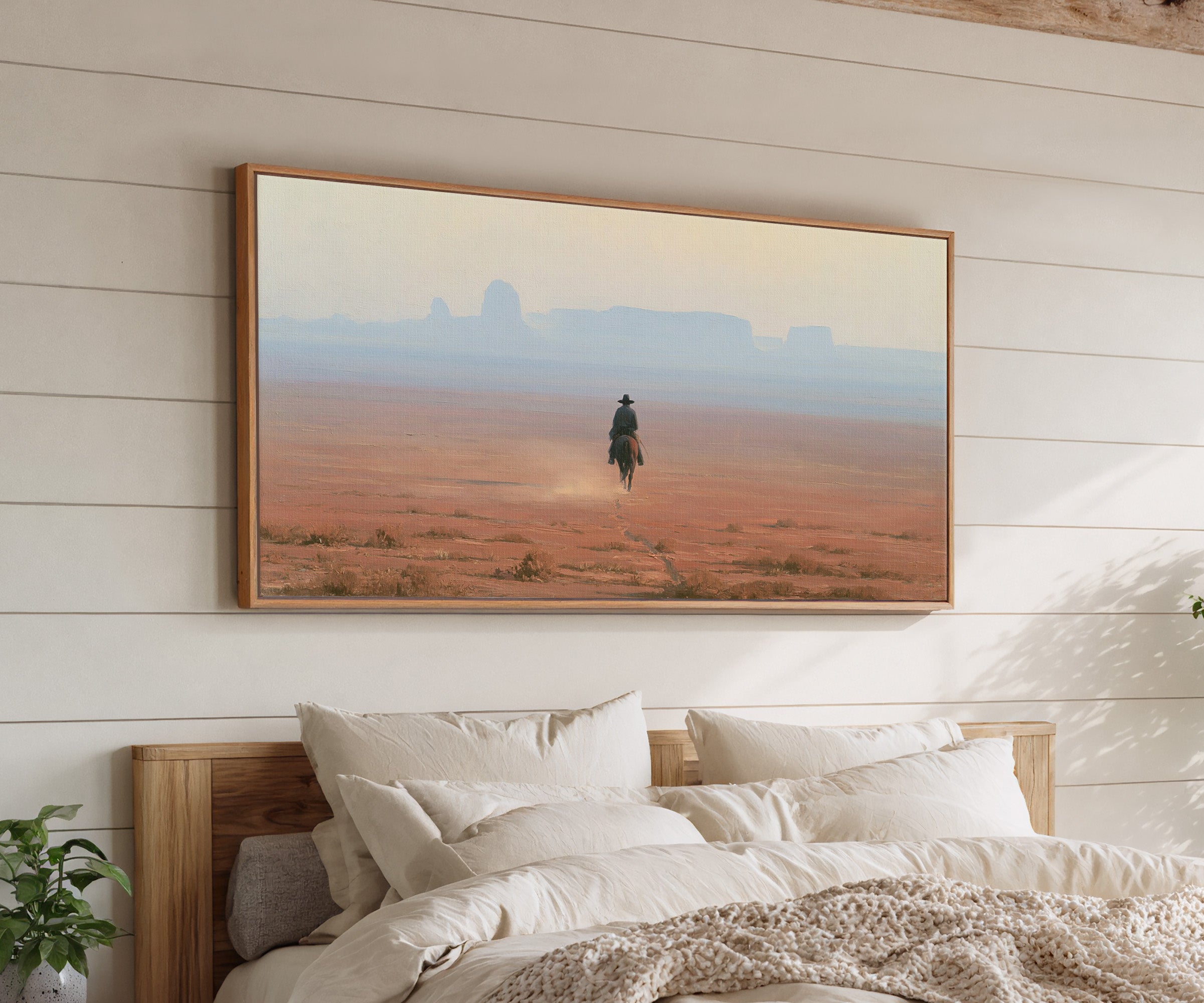 lone rider across a red desert plain with pale canvas wall art in an oak frame above a bed