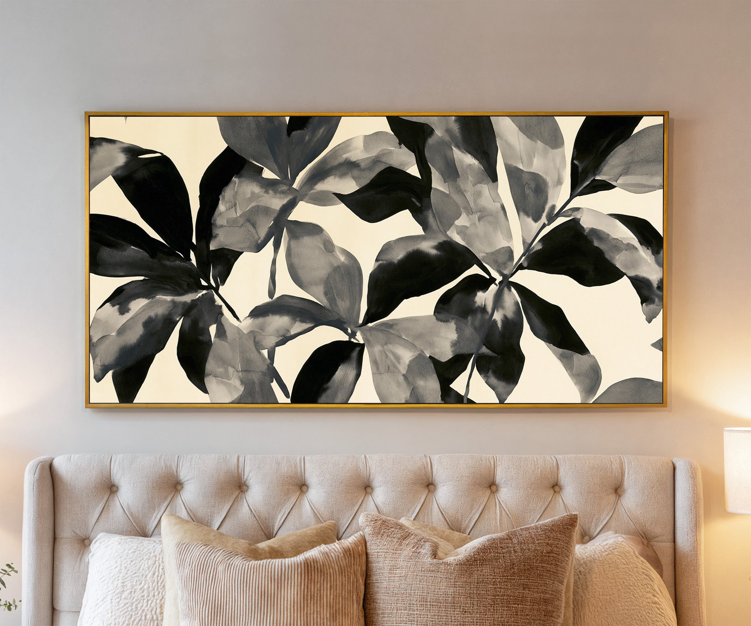 overlapping black and gray leaf shapes on cream canvas wall art in a gold frame above a bed