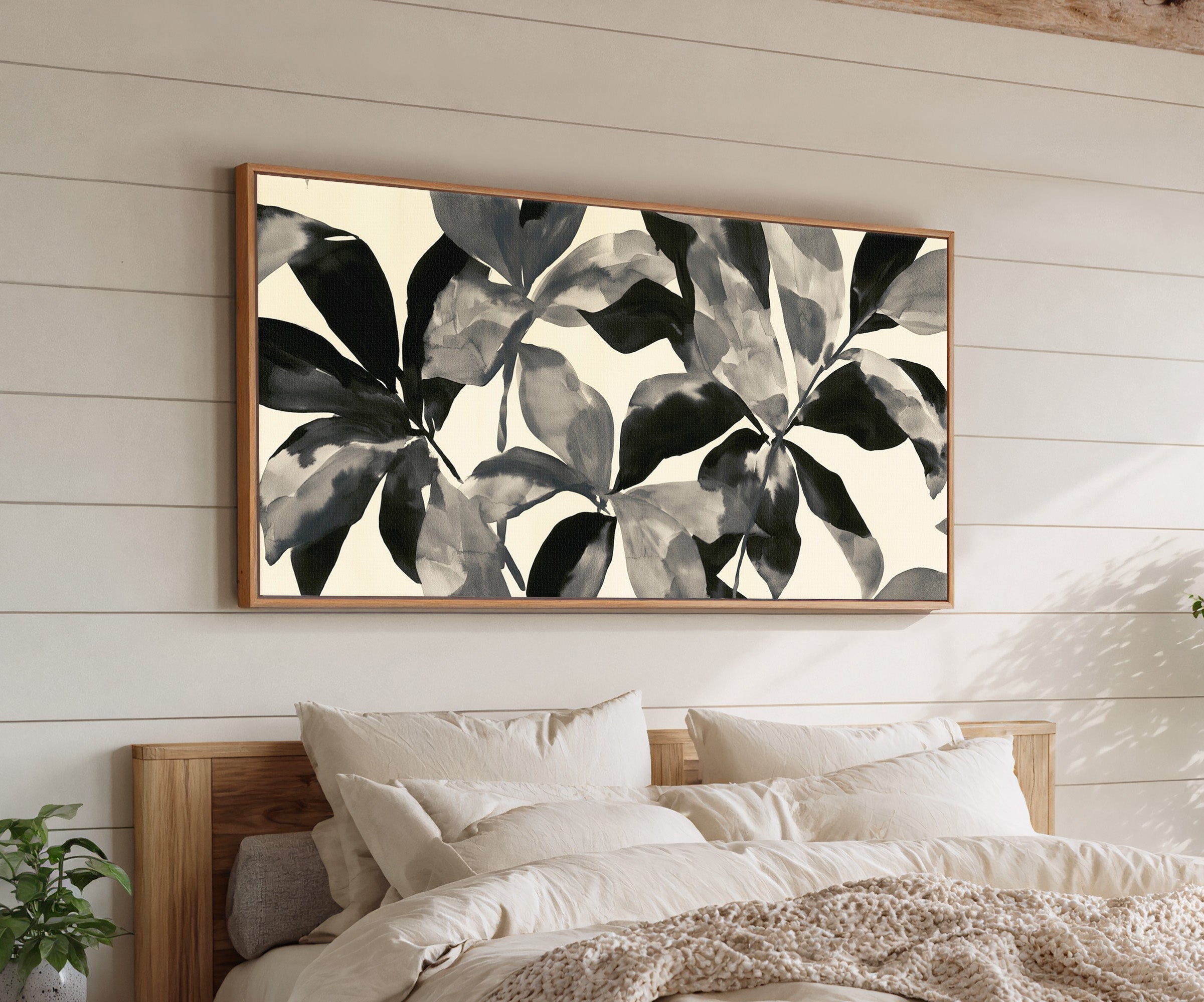 overlapping black and gray leaf shapes on cream canvas wall art in an oak frame above a bed